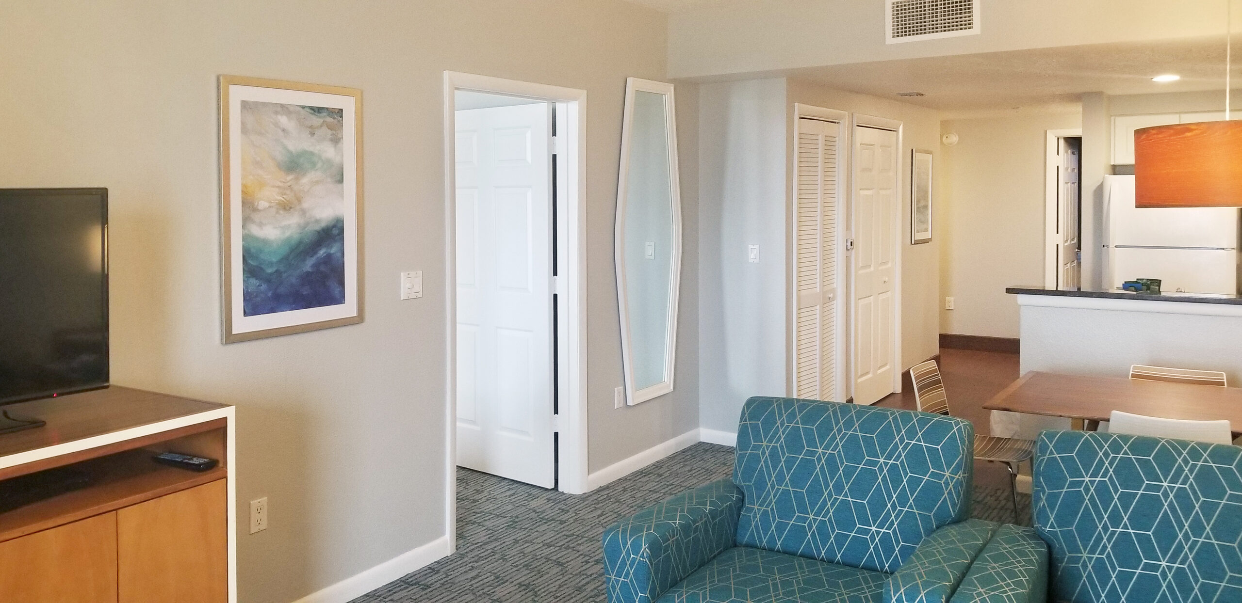 Renovated suite living area at Wyndham Ocean Walk with teal armchairs and open kitchen beyond