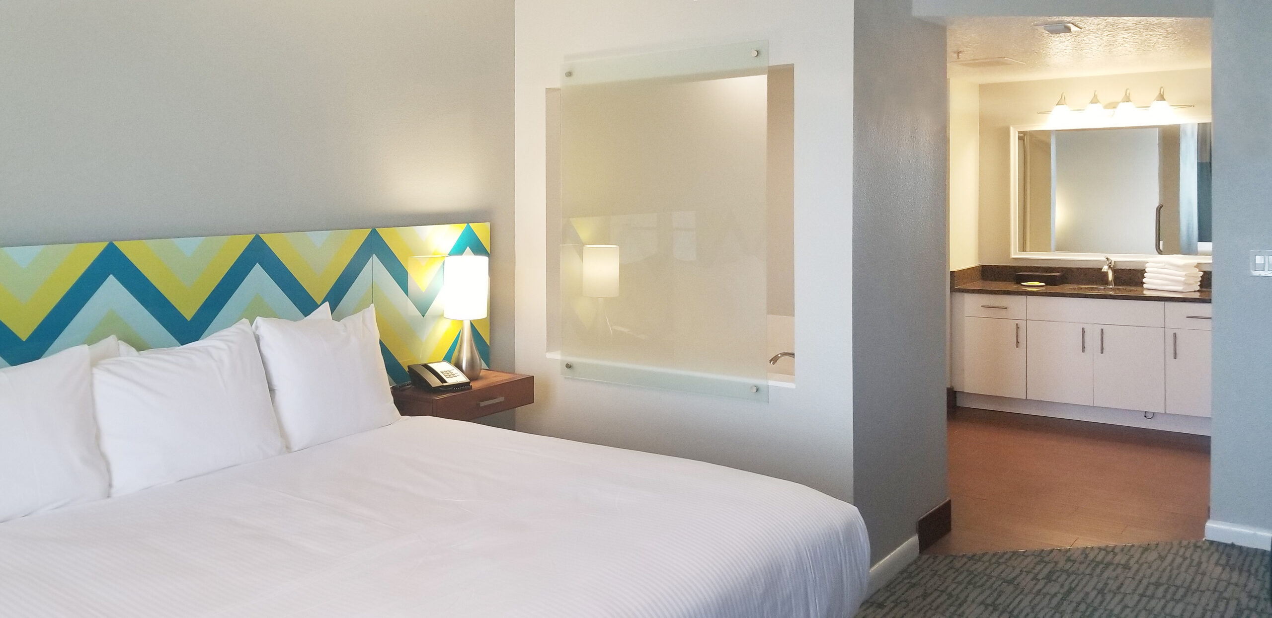 Renovated guestroom at Wyndham Ocean Walk with patterned headboard and vanity beyond